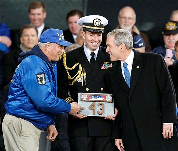 President Bush speaks to Mike Hallahan, president of the Intrepid Former Crew Members Association, while a naval attendant holds a piece of the deck of the Intrepid given as a gift to President Bush